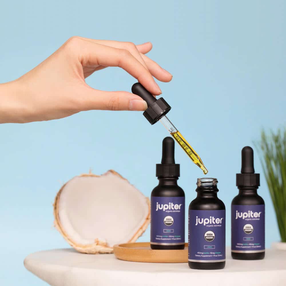 hand holding a tincture over Jupiter CBD bottles
